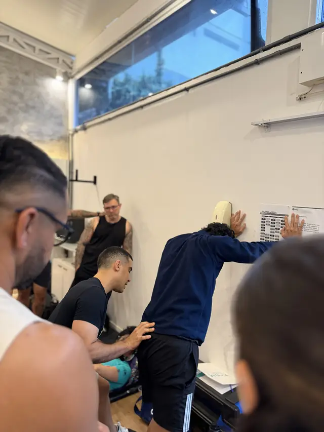 Igor ajusta a posição do quadril de um aluno apoiado na parede durante um teste