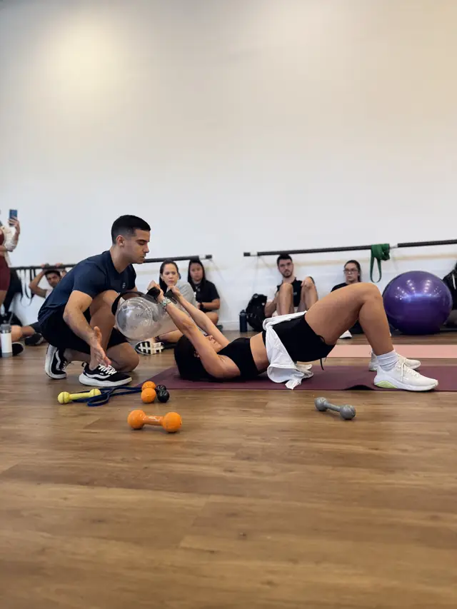 Igor orienta uma aluna em exercício de ponte com bolsa de água enquanto a turma observa